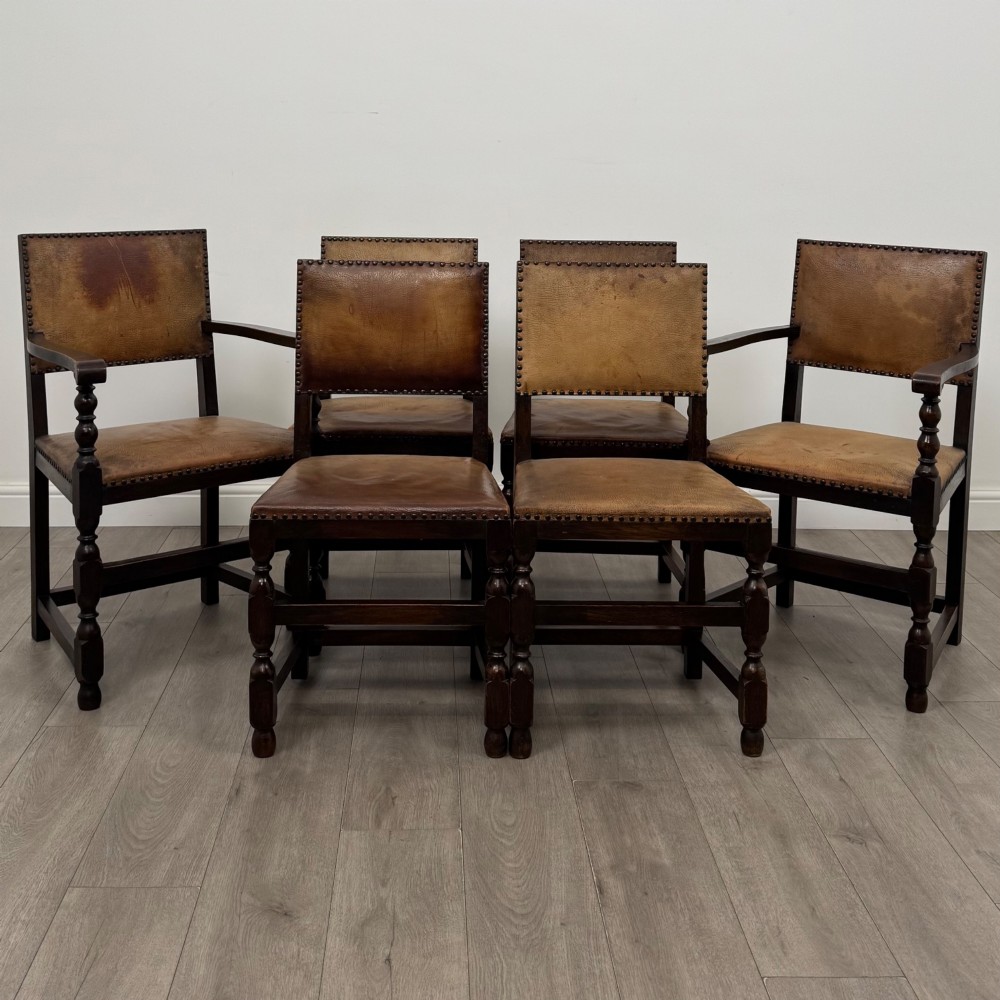 A set of six Edwardian dark oak dining chairs with tan studded leather upholstery, comprising two carver armchairs and four side chairs featuring turned legs.
