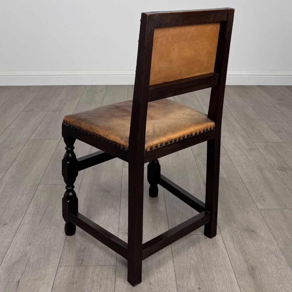 A set of six Edwardian dark oak dining chairs with tan studded leather upholstery, comprising two carver armchairs and four side chairs featuring turned legs. View IV
