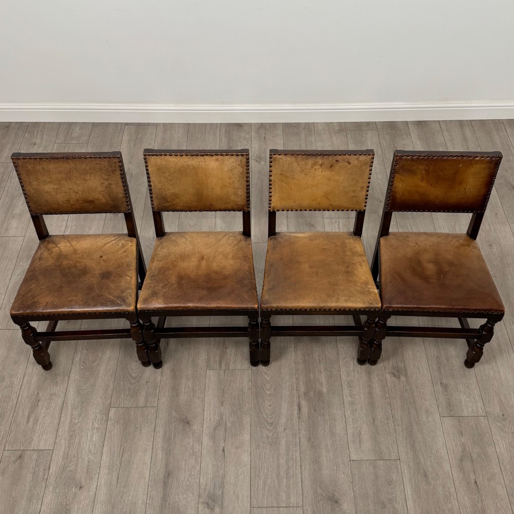 A set of six Edwardian dark oak dining chairs with tan studded leather upholstery, comprising two carver armchairs and four side chairs featuring turned legs. View X