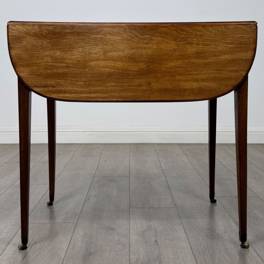 A 19th-century Georgian mahogany Pembroke table featuring two hinged drop-leaf sides, a single drawer with wooden knobs, and square tapered legs on brass castors. View II