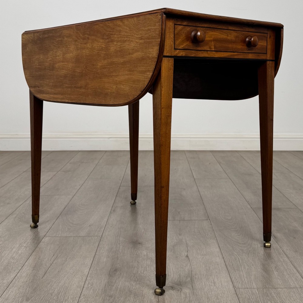 A 19th-century Georgian mahogany Pembroke table featuring two hinged drop-leaf sides, a single drawer with wooden knobs, and square tapered legs on brass castors. View III