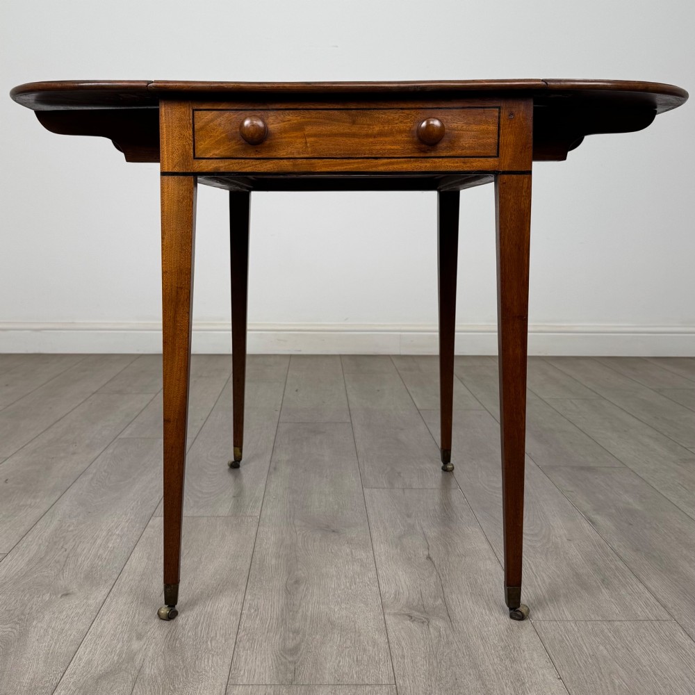 A 19th-century Georgian mahogany Pembroke table featuring two hinged drop-leaf sides, a single drawer with wooden knobs, and square tapered legs on brass castors. View V