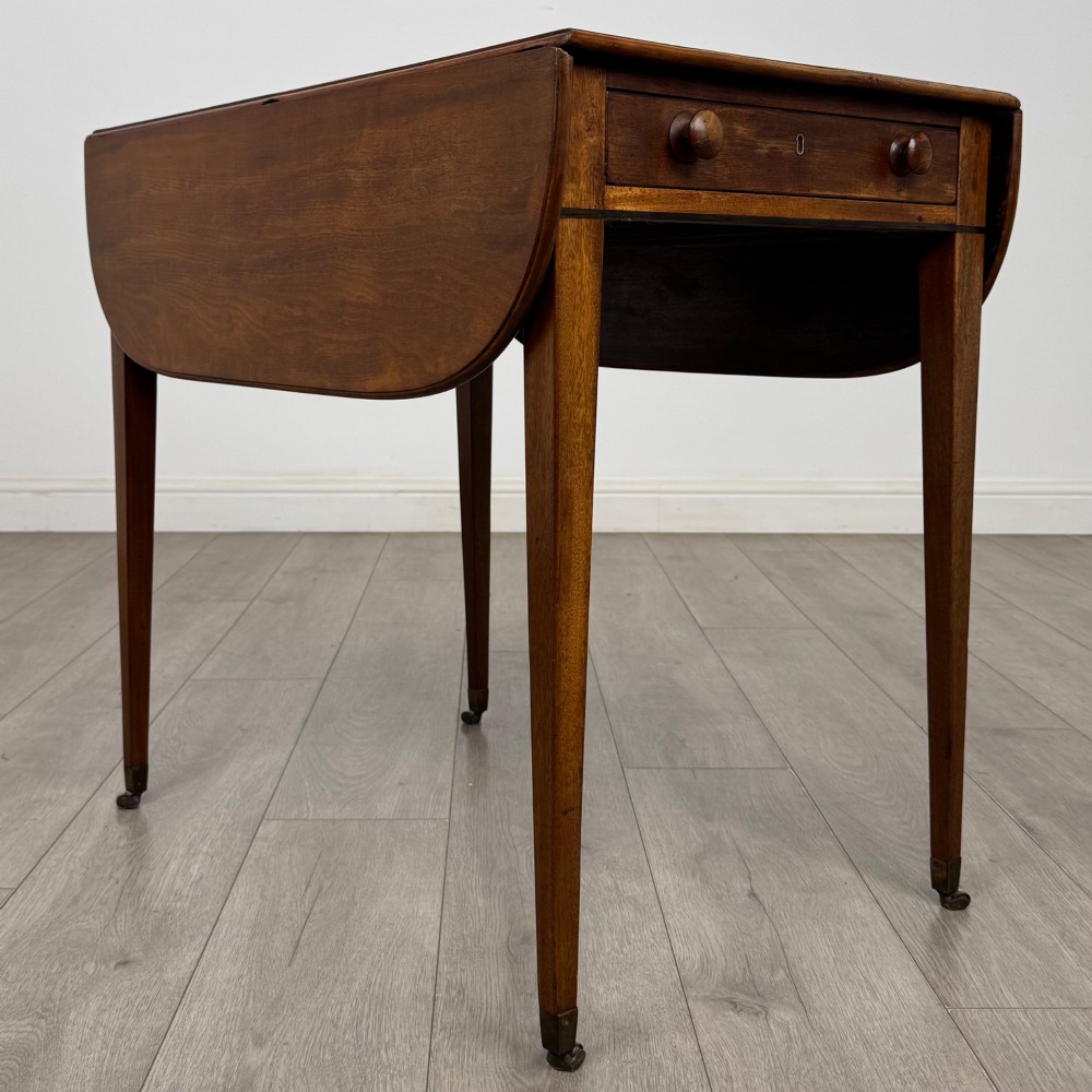 A 19th-century Georgian mahogany Pembroke table featuring two hinged drop-leaf sides, a single drawer with wooden knobs, and square tapered legs on brass castors. View VIII