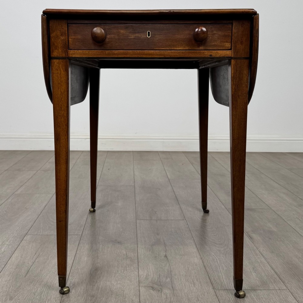 A 19th-century Georgian mahogany Pembroke table featuring two hinged drop-leaf sides, a single drawer with wooden knobs, and square tapered legs on brass castors. View IX