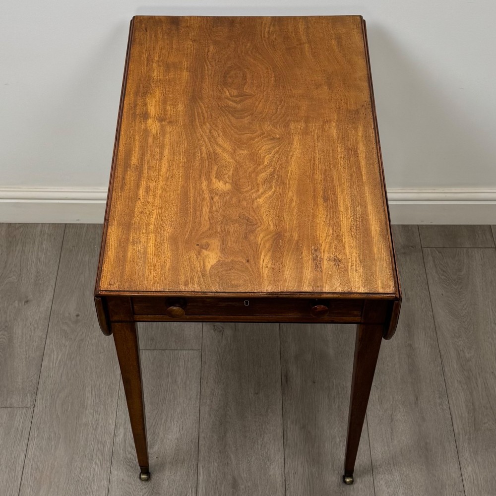 A 19th-century Georgian mahogany Pembroke table featuring two hinged drop-leaf sides, a single drawer with wooden knobs, and square tapered legs on brass castors. View X