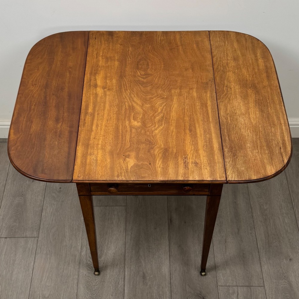 A 19th-century Georgian mahogany Pembroke table featuring two hinged drop-leaf sides, a single drawer with wooden knobs, and square tapered legs on brass castors. View XI