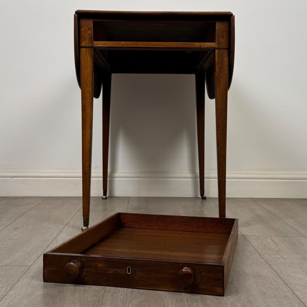 A 19th-century Georgian mahogany Pembroke table featuring two hinged drop-leaf sides, a single drawer with wooden knobs, and square tapered legs on brass castors. View XII