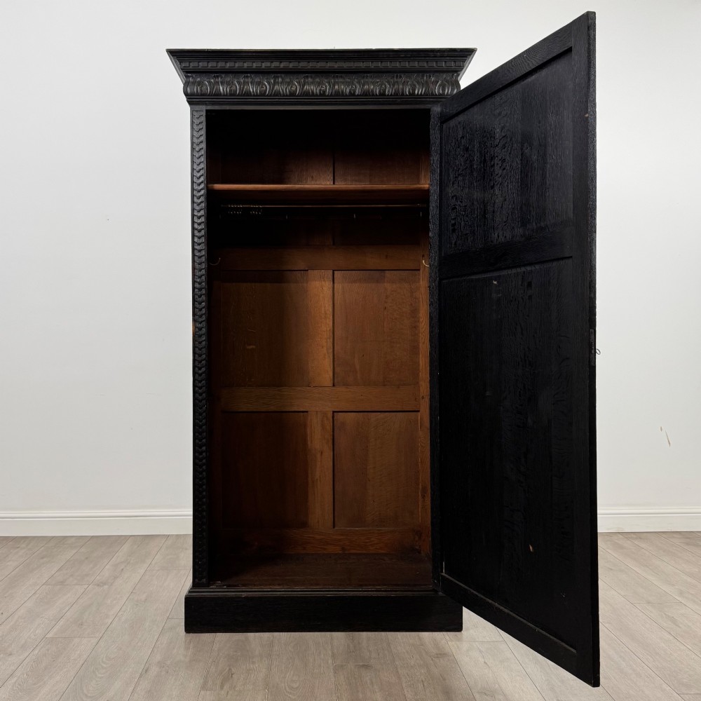 A single-door dark oak Victorian wardrobe featuring geometric panel mouldings, a carved relief face in a central diamond, and a pronounced decorative cornice. View II