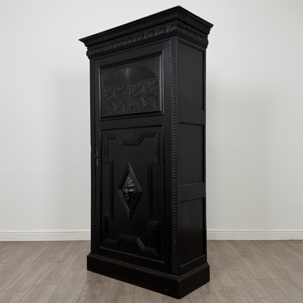 A single-door dark oak Victorian wardrobe featuring geometric panel mouldings, a carved relief face in a central diamond, and a pronounced decorative cornice. View III