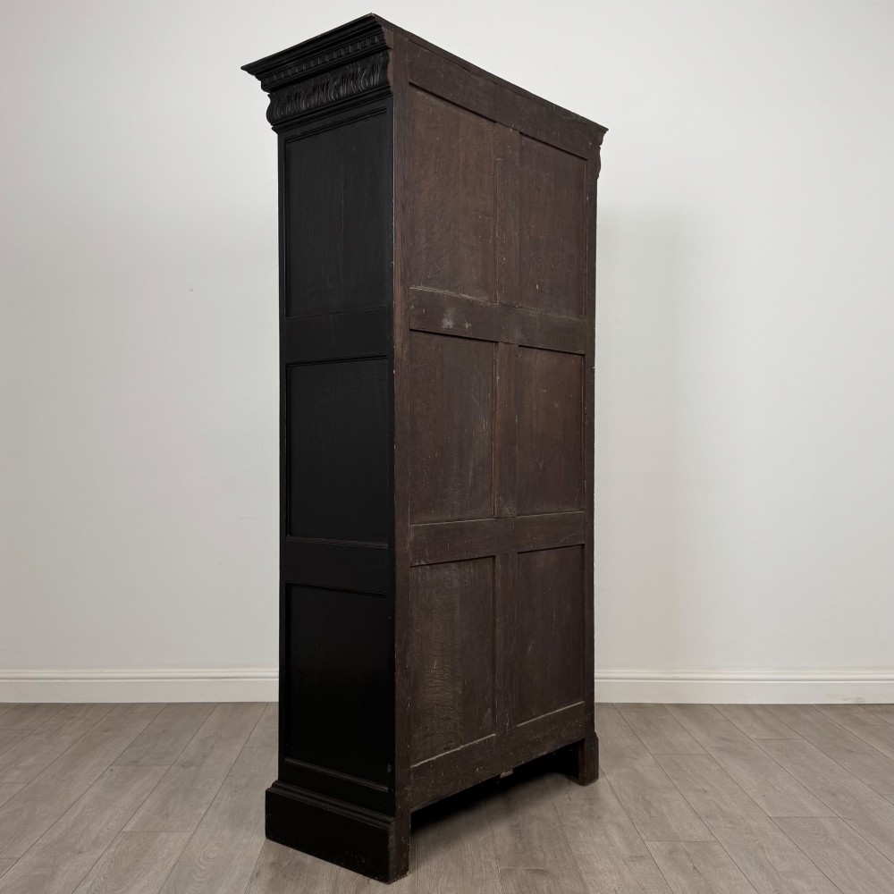 A single-door dark oak Victorian wardrobe featuring geometric panel mouldings, a carved relief face in a central diamond, and a pronounced decorative cornice. View V