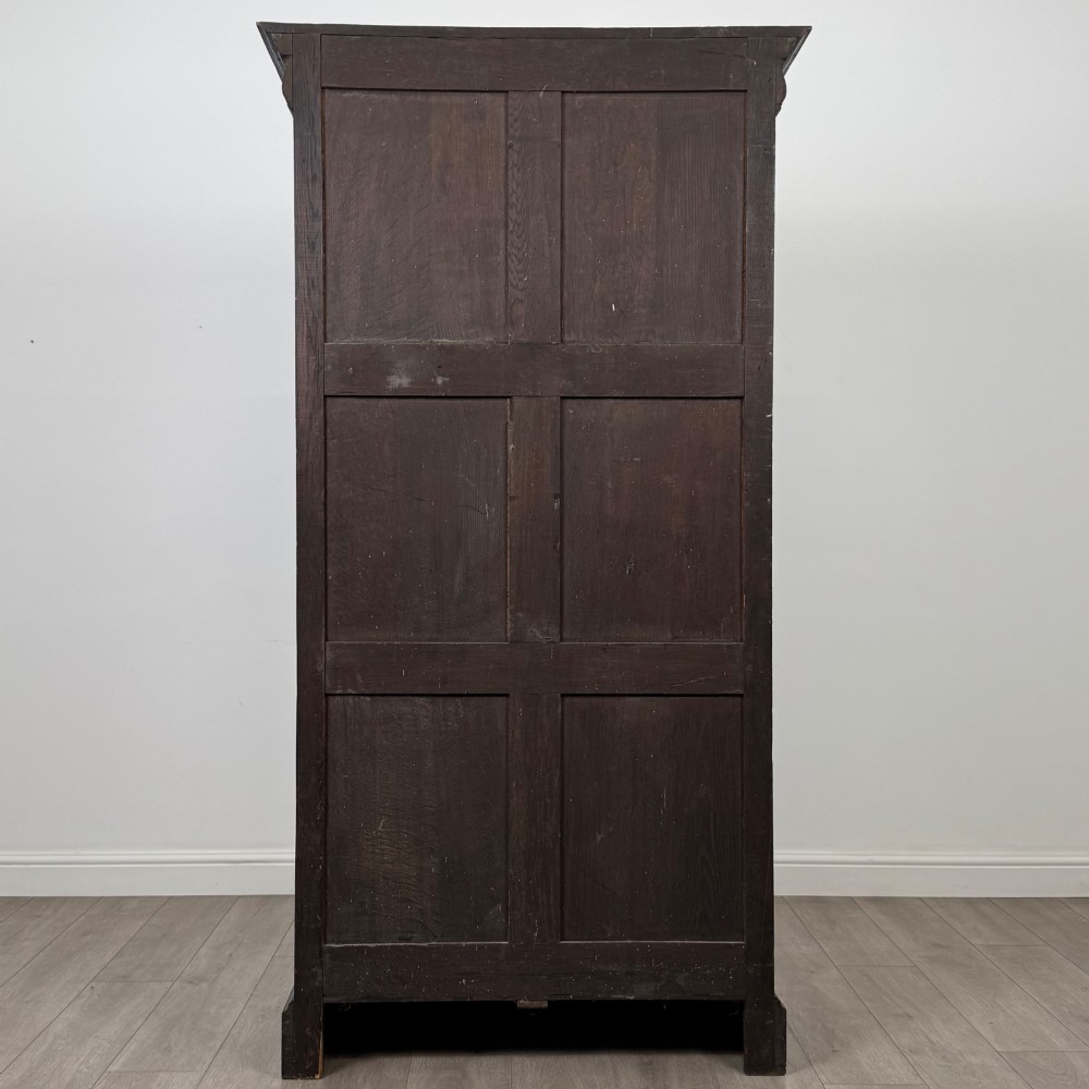 A single-door dark oak Victorian wardrobe featuring geometric panel mouldings, a carved relief face in a central diamond, and a pronounced decorative cornice. View VI