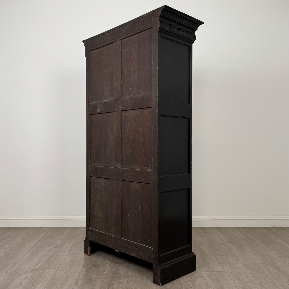 A single-door dark oak Victorian wardrobe featuring geometric panel mouldings, a carved relief face in a central diamond, and a pronounced decorative cornice. View VII