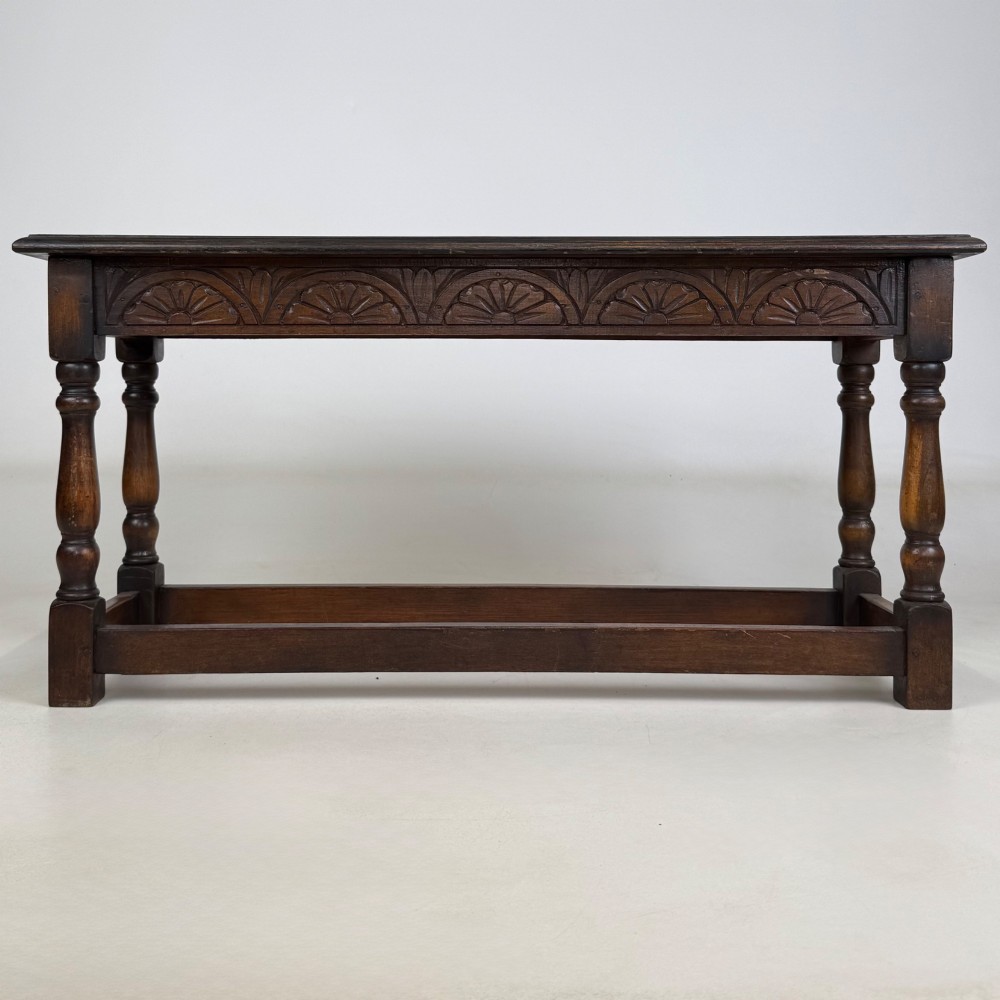 A dark carved oak bench featuring turned legs, a lower box stretcher, and a carved lunette frieze along the apron.