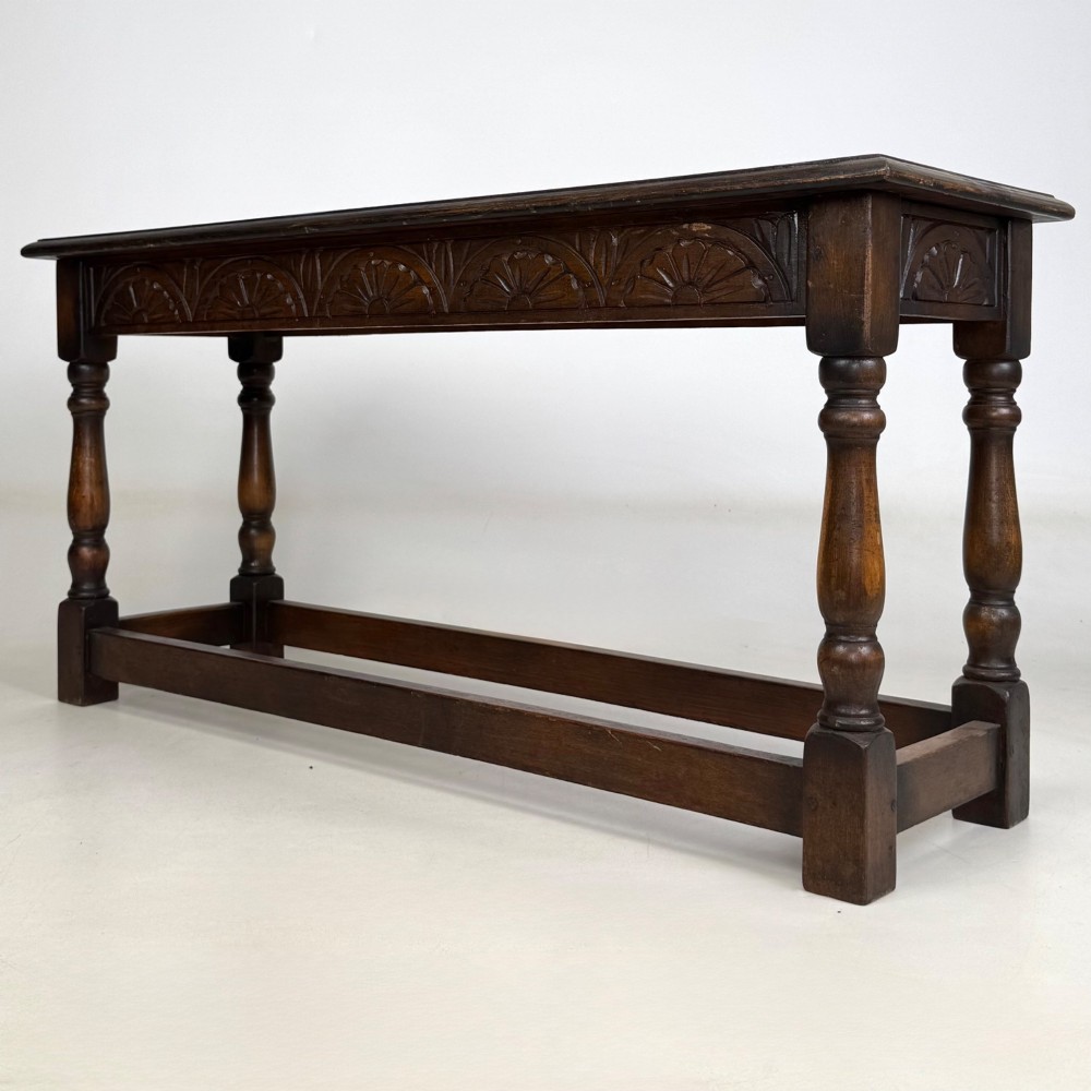 A dark carved oak bench featuring turned legs, a lower box stretcher, and a carved lunette frieze along the apron. View II