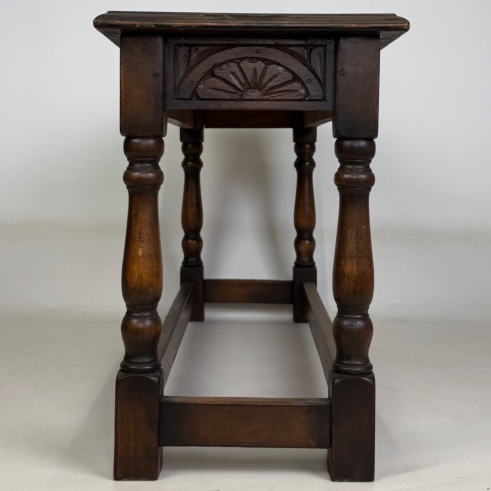 A dark carved oak bench featuring turned legs, a lower box stretcher, and a carved lunette frieze along the apron. View III