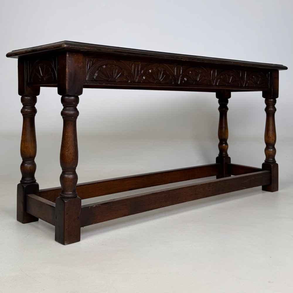 A dark carved oak bench featuring turned legs, a lower box stretcher, and a carved lunette frieze along the apron. View IV