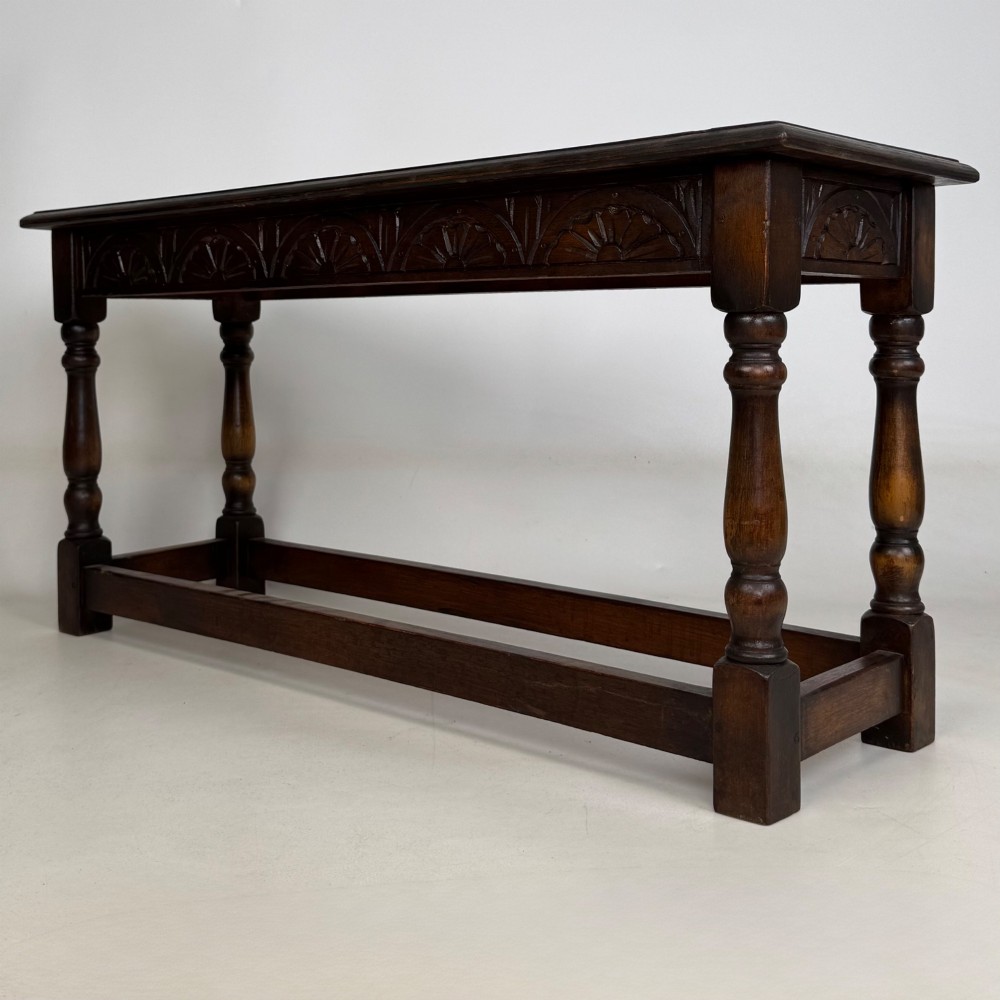 A dark carved oak bench featuring turned legs, a lower box stretcher, and a carved lunette frieze along the apron. View VI
