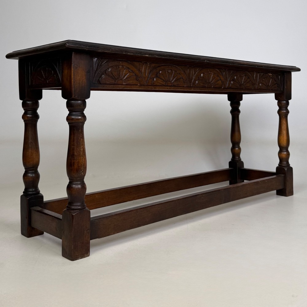 A dark carved oak bench featuring turned legs, a lower box stretcher, and a carved lunette frieze along the apron. View VIII