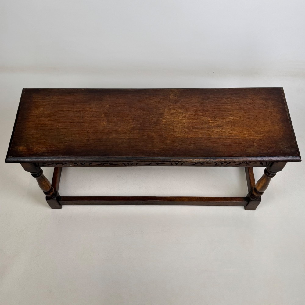 A dark carved oak bench featuring turned legs, a lower box stretcher, and a carved lunette frieze along the apron. View IX