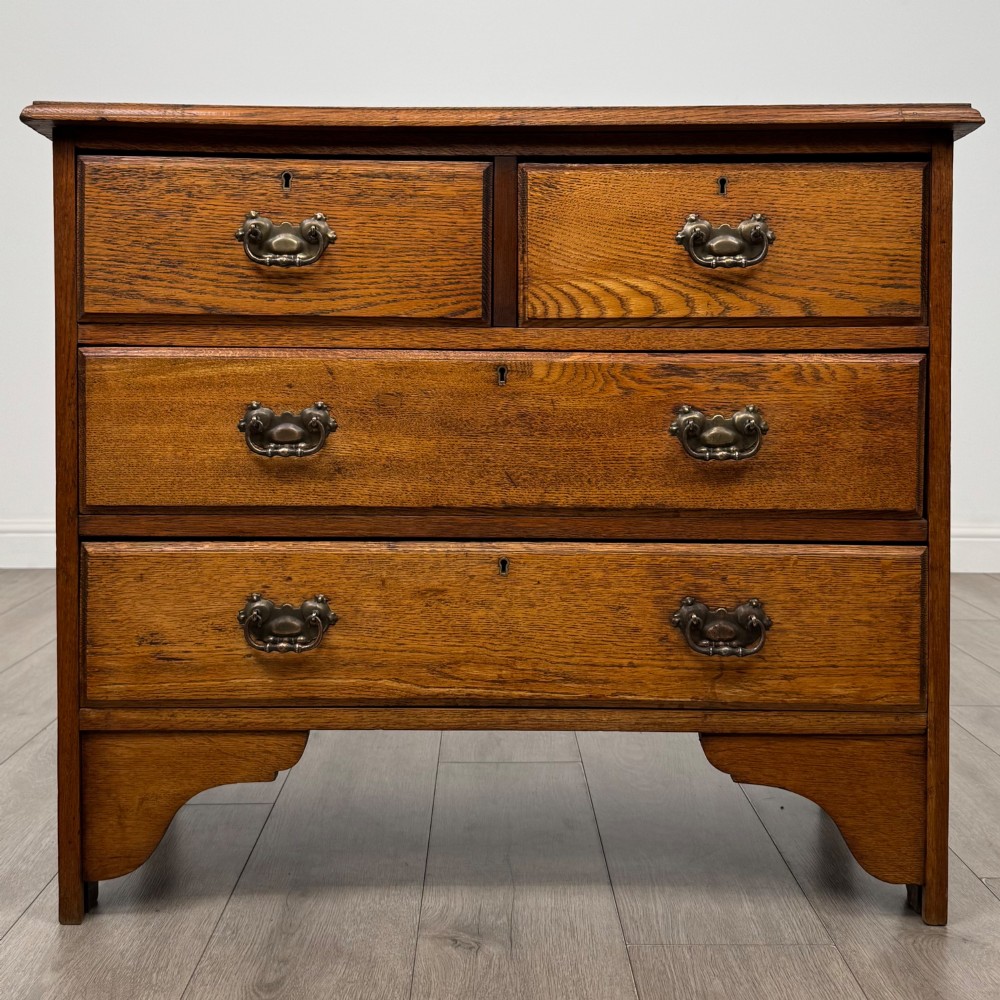 An Edwardian warm brown oak chest of drawers featuring two short upper drawers and two long lower drawers with brass drop handles.