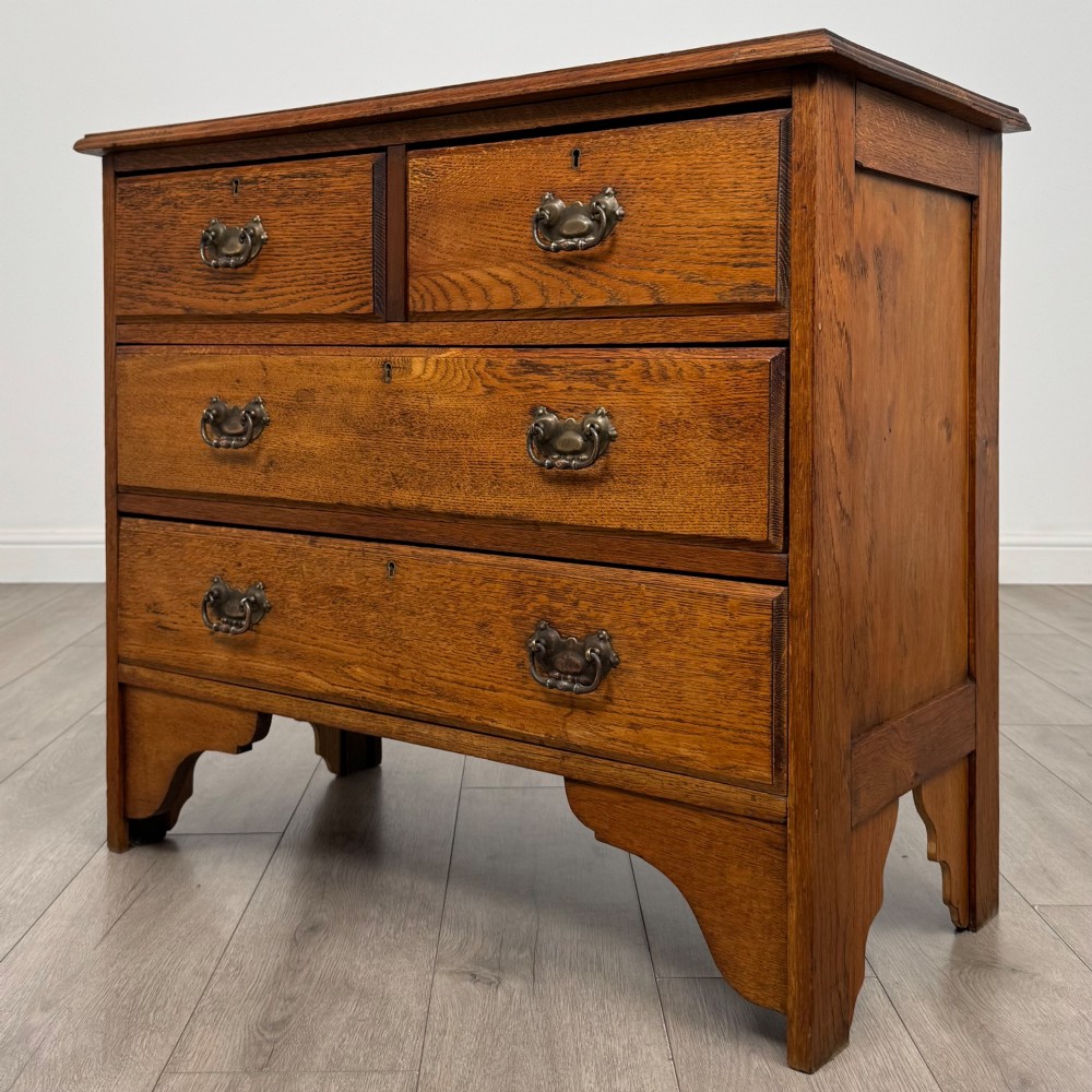 An Edwardian warm brown oak chest of drawers featuring two short upper drawers and two long lower drawers with brass drop handles. View II