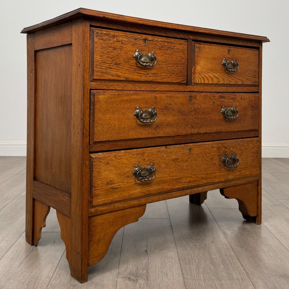 An Edwardian warm brown oak chest of drawers featuring two short upper drawers and two long lower drawers with brass drop handles. View VIII