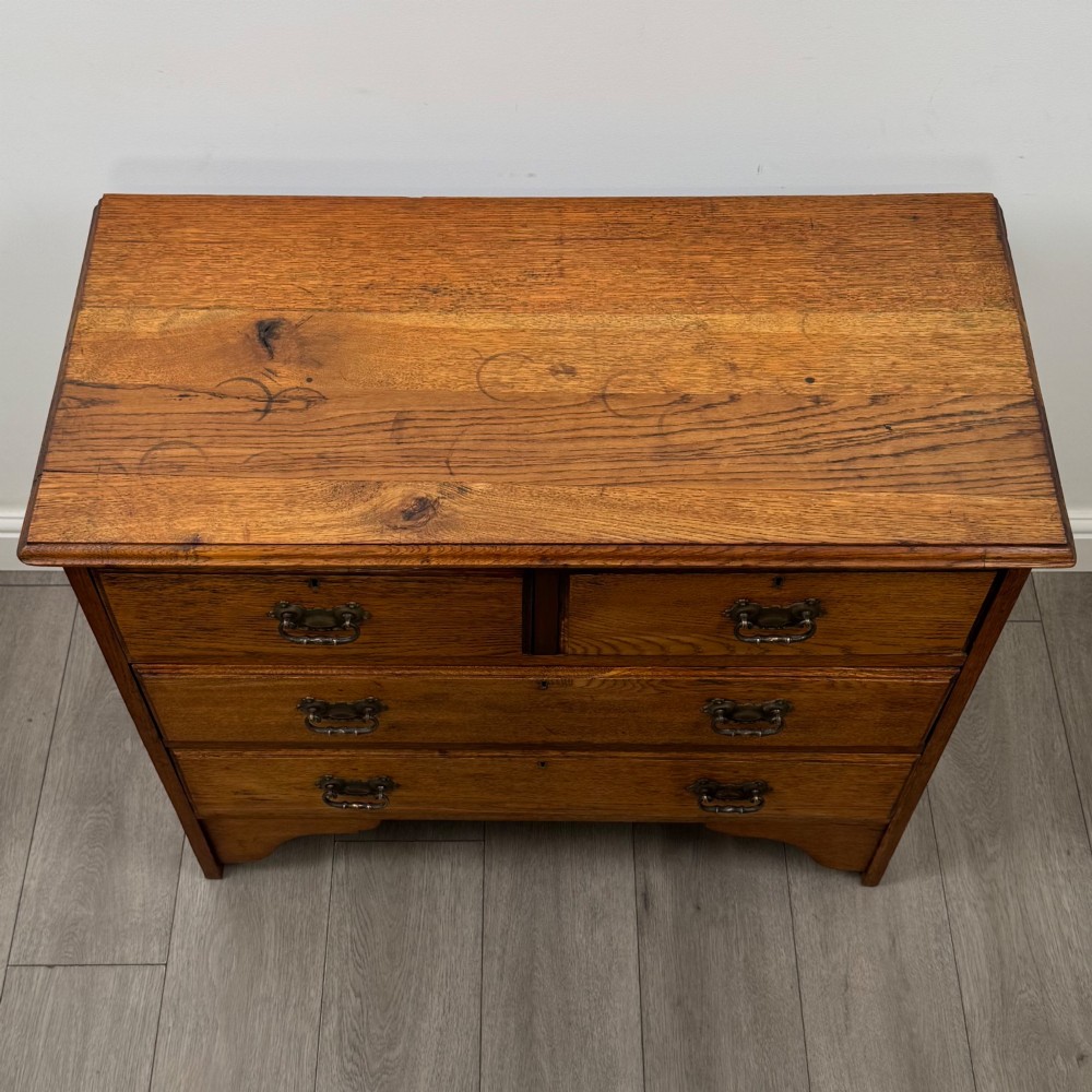 An Edwardian warm brown oak chest of drawers featuring two short upper drawers and two long lower drawers with brass drop handles. View IX