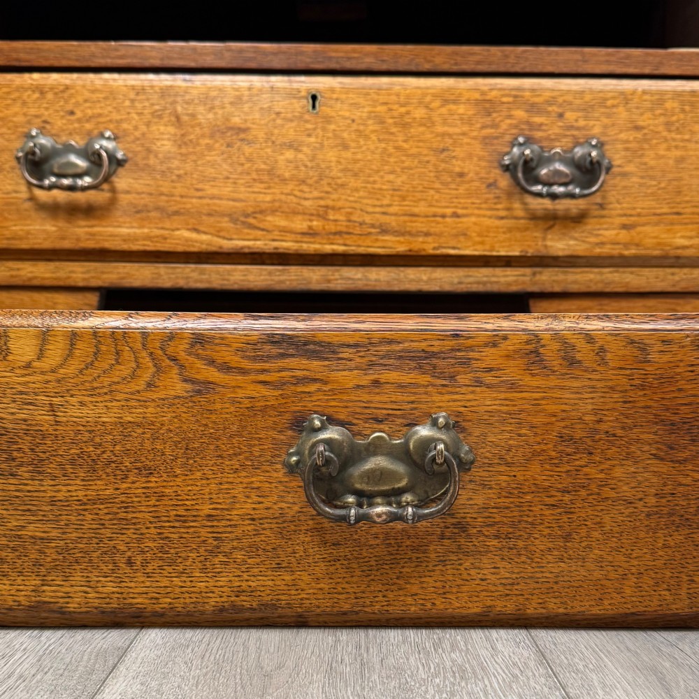 An Edwardian warm brown oak chest of drawers featuring two short upper drawers and two long lower drawers with brass drop handles. View XI