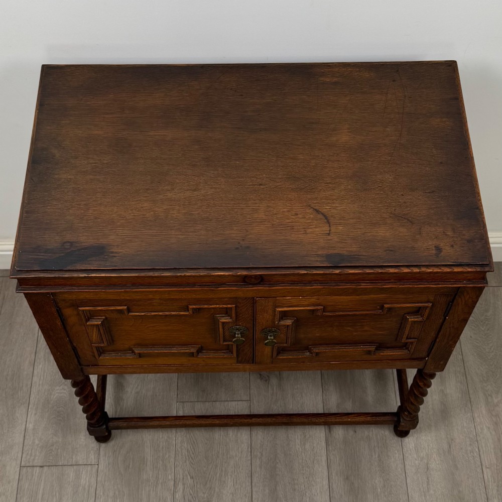 A dark oak Jacobean style cabinet featuring two doors with geometric fielded panels, twin brass drop handles, and four barley twist legs supported by low stretchers. View X