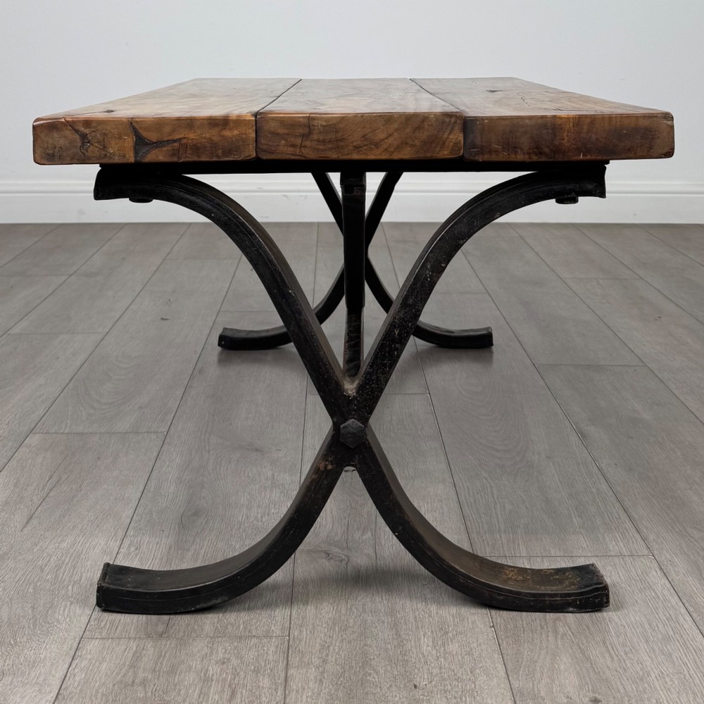A low rectangular coffee table featuring a thick hardwood plank top set upon a dark curved iron X-frame base. View II