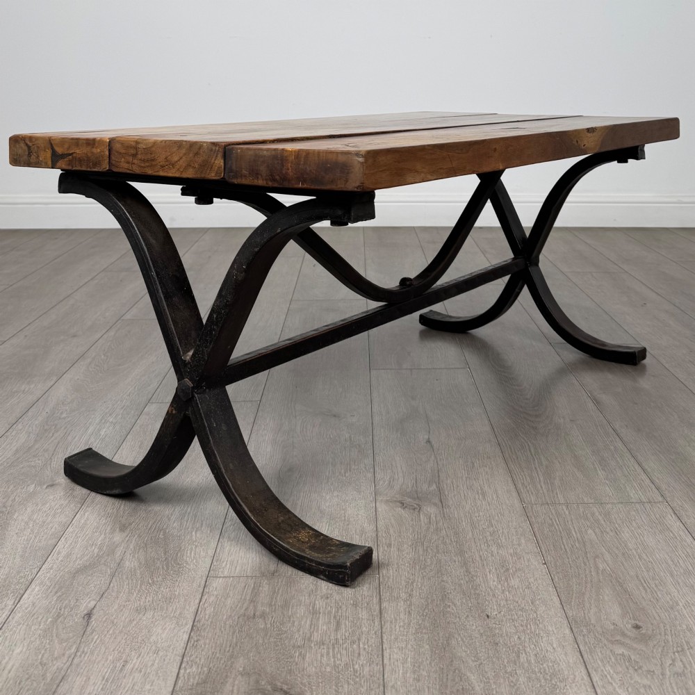 A low rectangular coffee table featuring a thick hardwood plank top set upon a dark curved iron X-frame base. View III