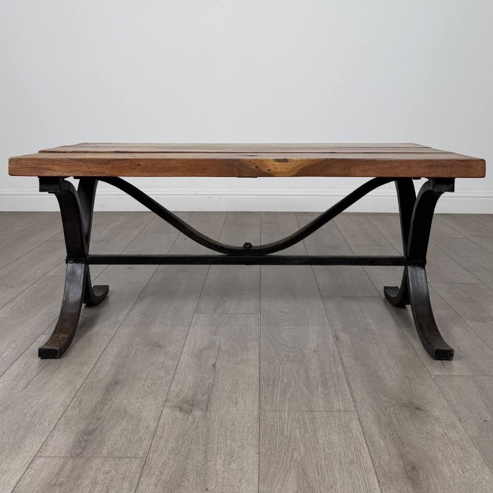A low rectangular coffee table featuring a thick hardwood plank top set upon a dark curved iron X-frame base. View IV