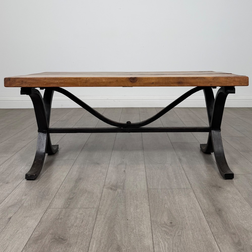 A low rectangular coffee table featuring a thick hardwood plank top set upon a dark curved iron X-frame base. View VIII