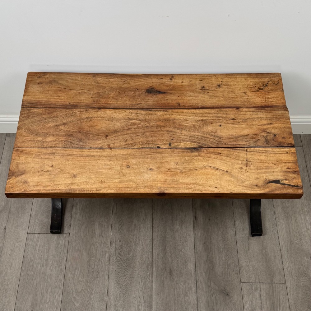 A low rectangular coffee table featuring a thick hardwood plank top set upon a dark curved iron X-frame base. View IX