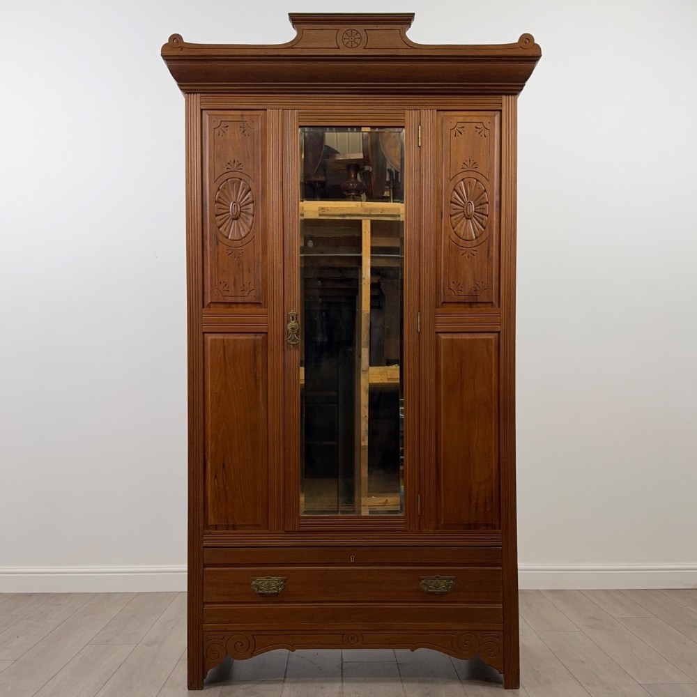 An Edwardian walnut wardrobe featuring a central mirrored door flanked by carved timber panels above a single base drawer.