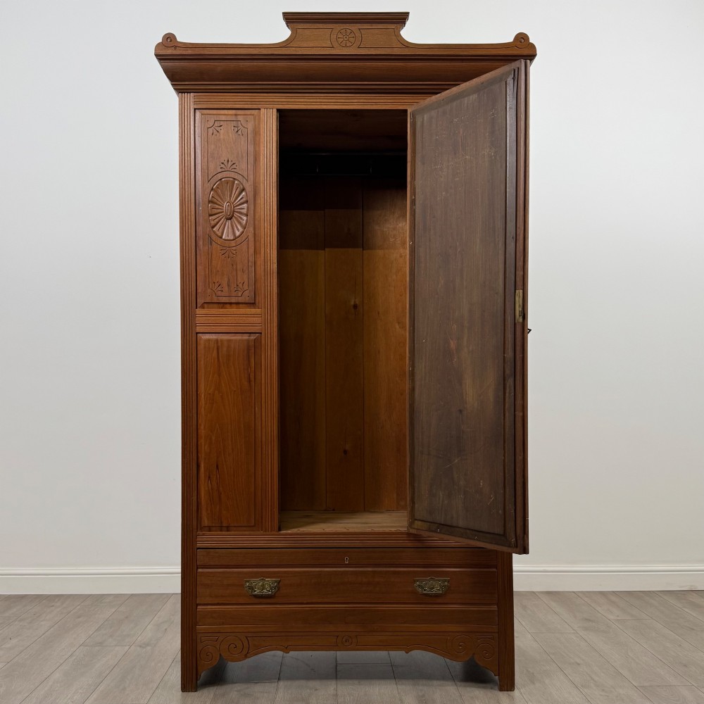 An Edwardian walnut wardrobe featuring a central mirrored door flanked by carved timber panels above a single base drawer. View II