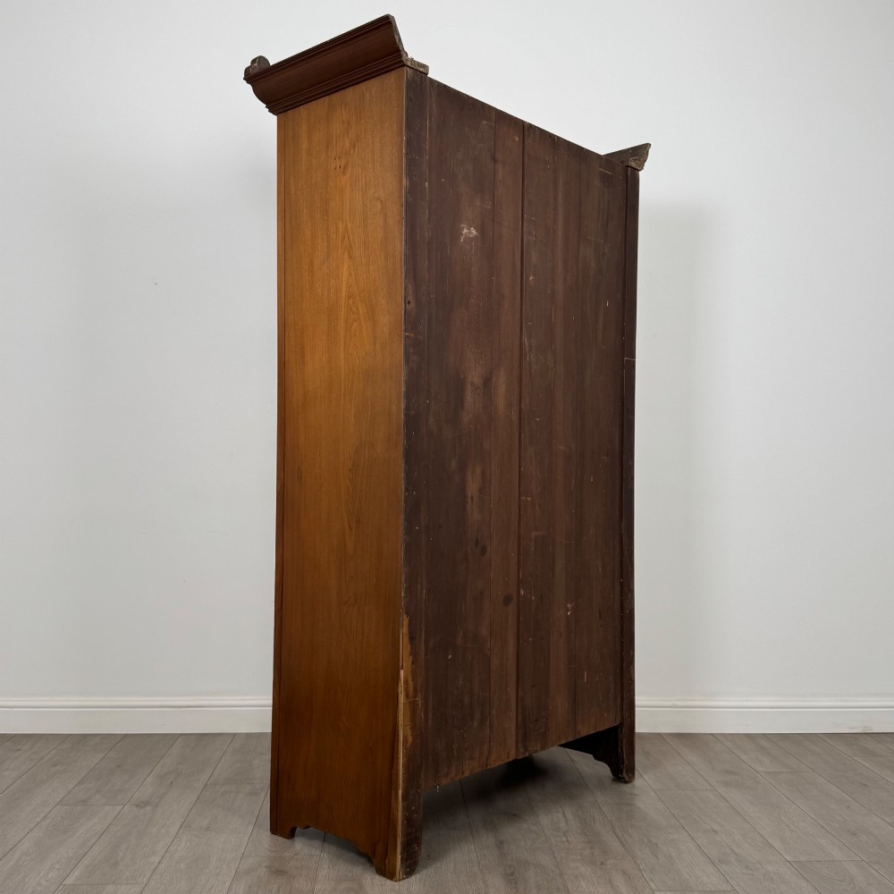 An Edwardian walnut wardrobe featuring a central mirrored door flanked by carved timber panels above a single base drawer. View V