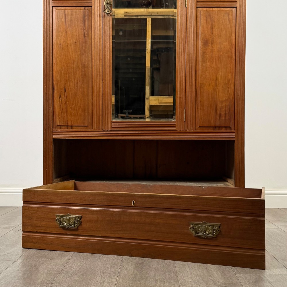 An Edwardian walnut wardrobe featuring a central mirrored door flanked by carved timber panels above a single base drawer. View X