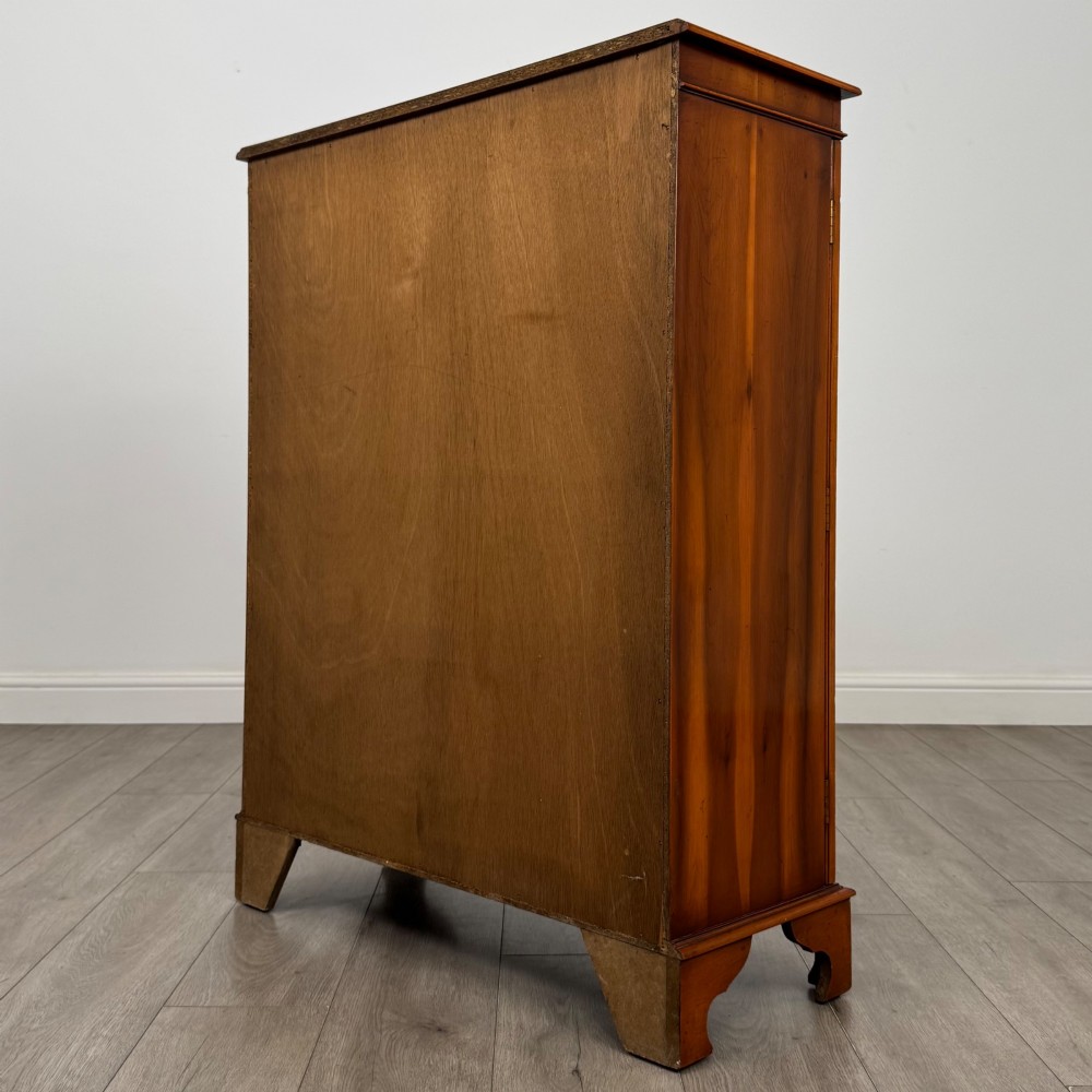 An antique yew wood display cabinet featuring two astragal glazed doors with geometric glazing bars, housing books on internal shelves, and resting on bracket feet. View VIII
