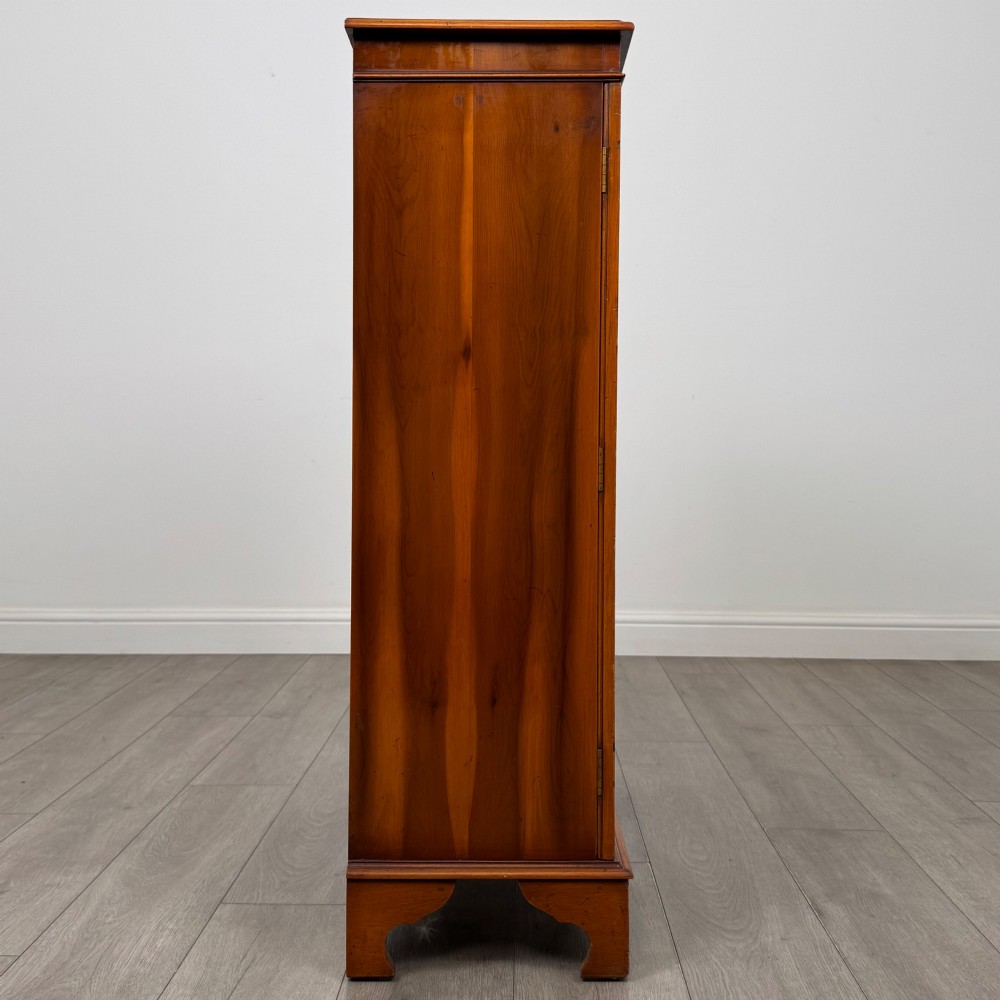 An antique yew wood display cabinet featuring two astragal glazed doors with geometric glazing bars, housing books on internal shelves, and resting on bracket feet. View IX