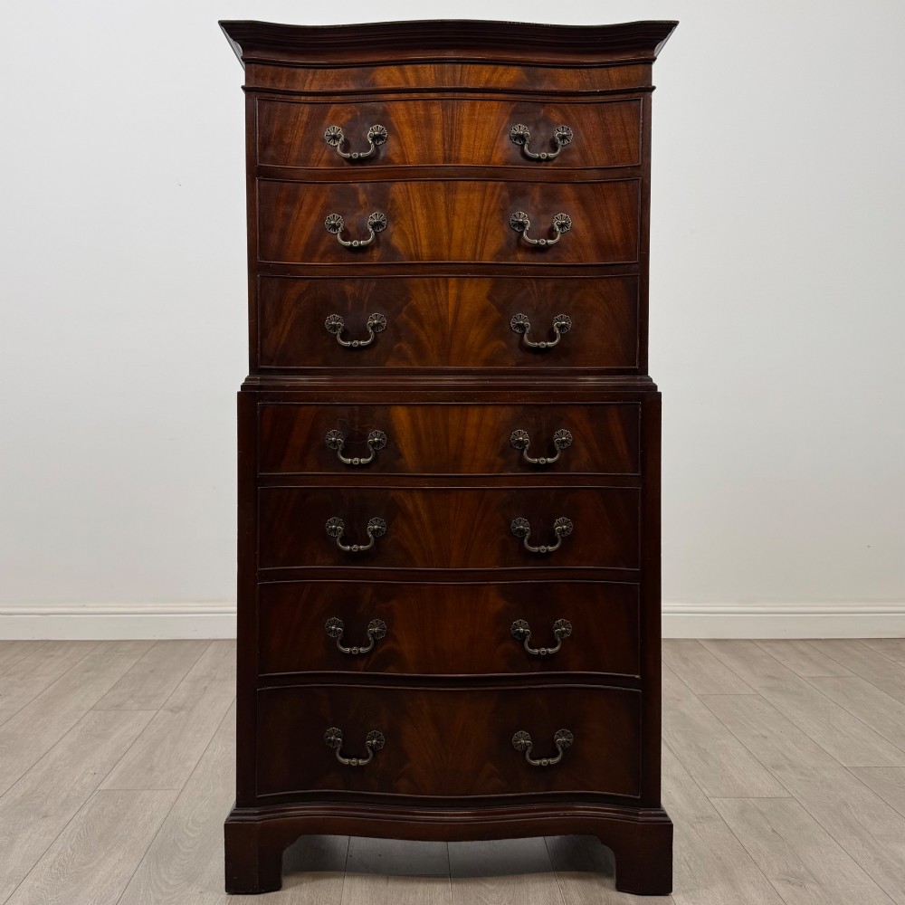 A tall 20th-century mahogany serpentine chest of drawers featuring seven graduated drawers with brass handles and bracket feet.
