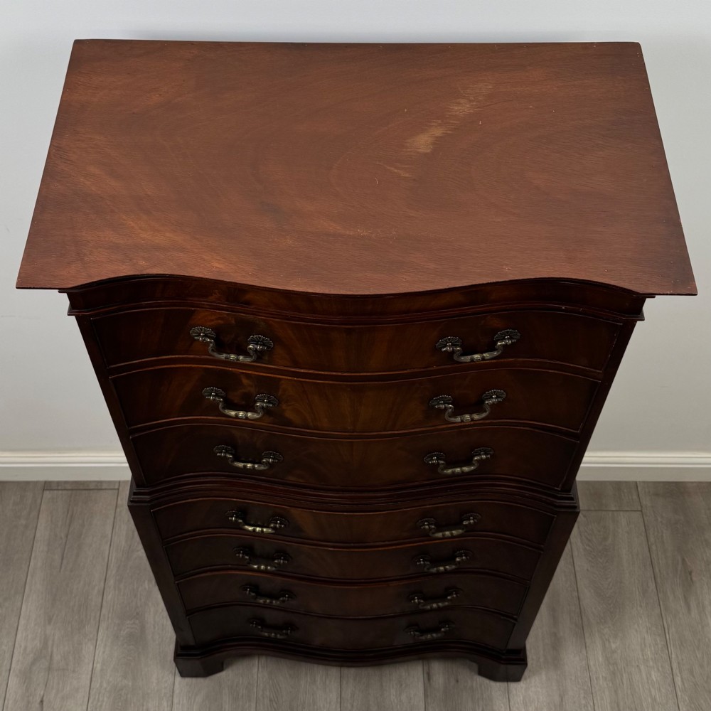 A tall 20th-century mahogany serpentine chest of drawers featuring seven graduated drawers with brass handles and bracket feet. View IX