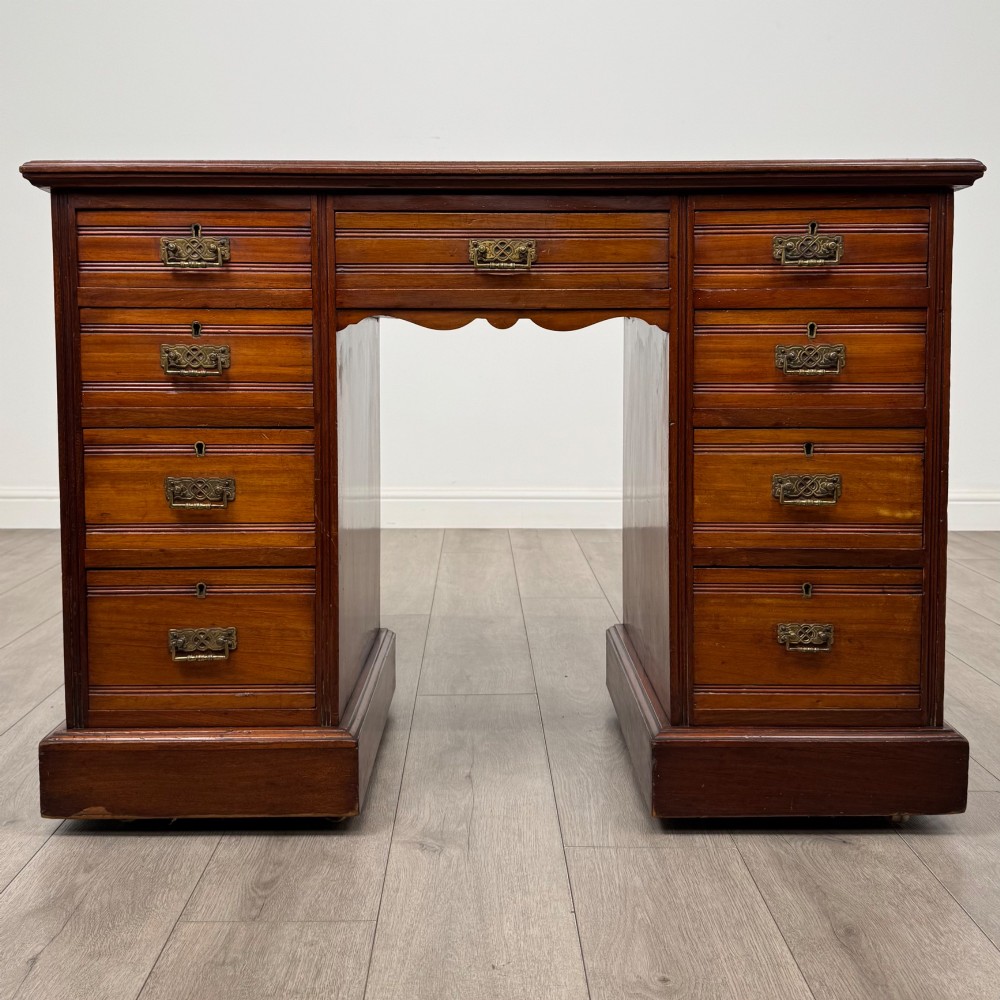 An Edwardian mahogany pedestal desk featuring nine reeded drawers with decorative brass drop handles and a central kneehole.