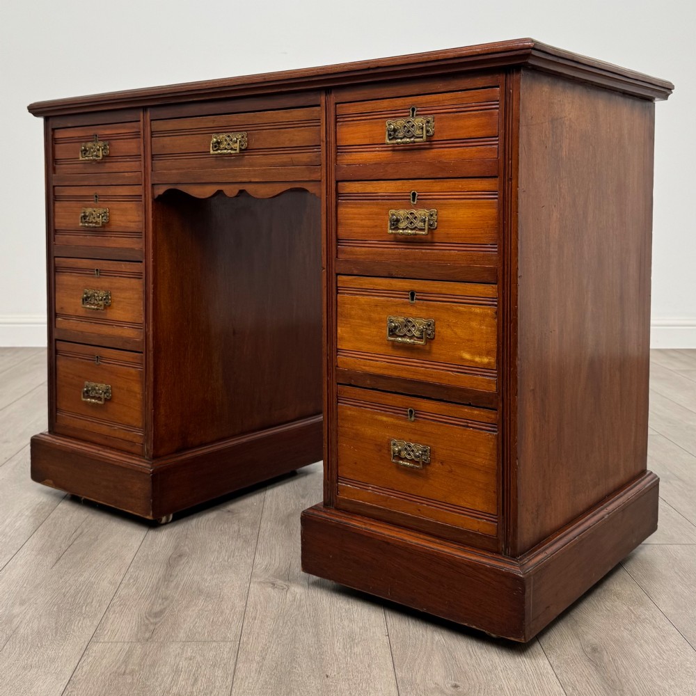 An Edwardian mahogany pedestal desk featuring nine reeded drawers with decorative brass drop handles and a central kneehole. View II