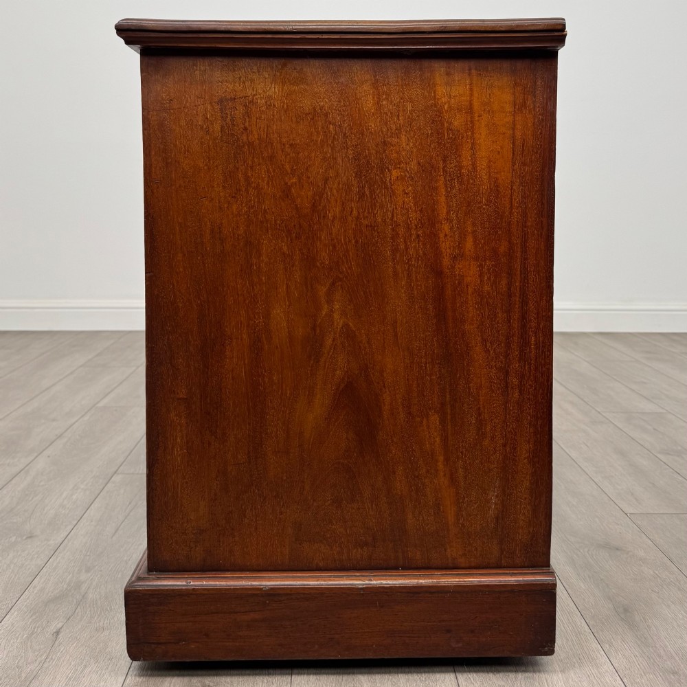 An Edwardian mahogany pedestal desk featuring nine reeded drawers with decorative brass drop handles and a central kneehole. View III