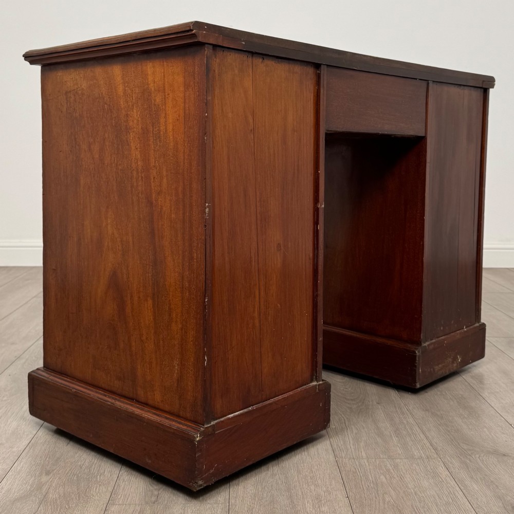 An Edwardian mahogany pedestal desk featuring nine reeded drawers with decorative brass drop handles and a central kneehole. View IV