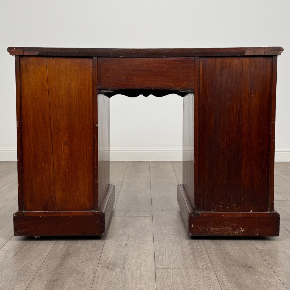 An Edwardian mahogany pedestal desk featuring nine reeded drawers with decorative brass drop handles and a central kneehole. View V