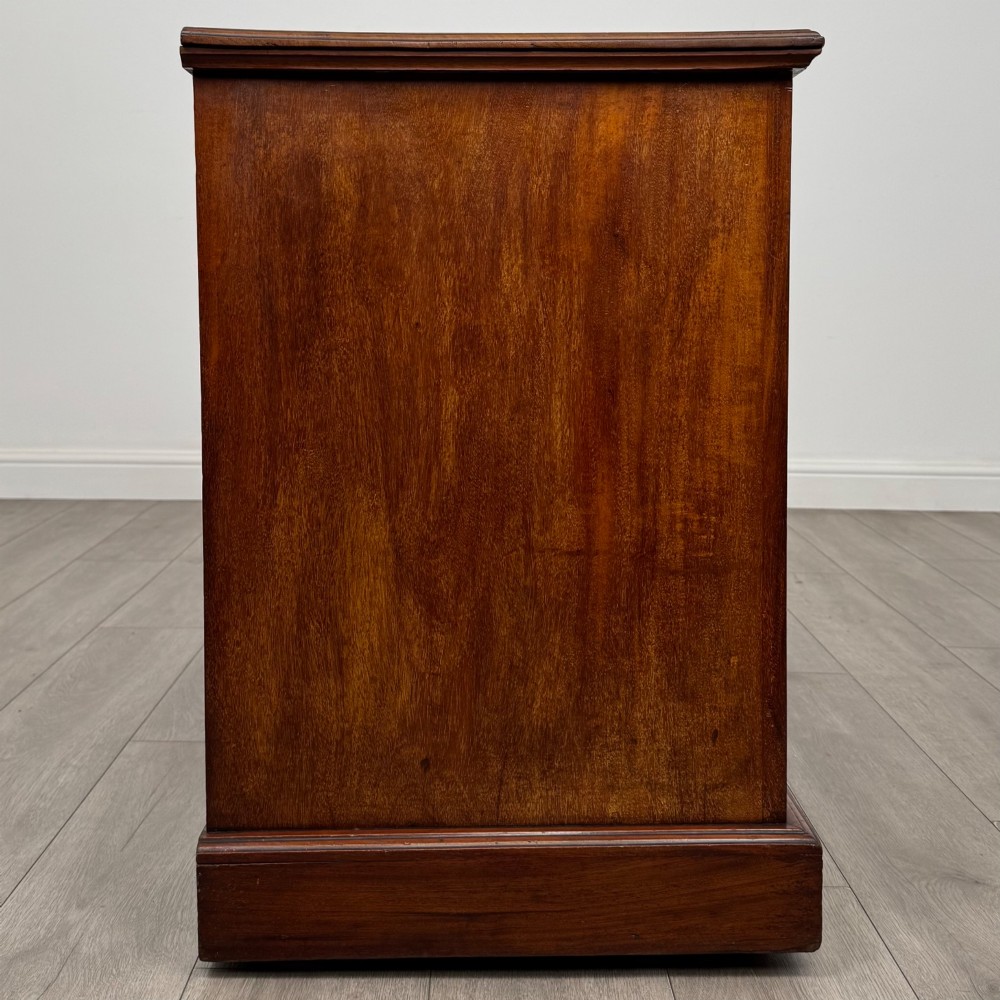 An Edwardian mahogany pedestal desk featuring nine reeded drawers with decorative brass drop handles and a central kneehole. View VII