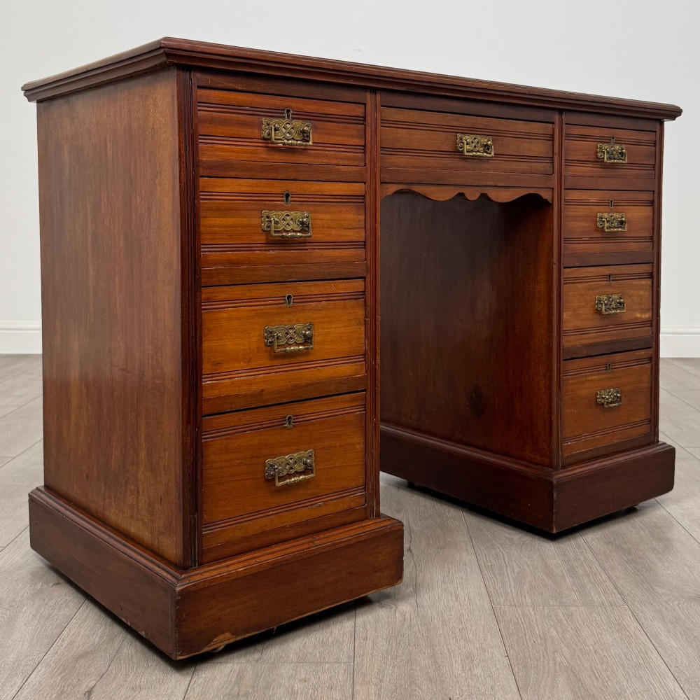 An Edwardian mahogany pedestal desk featuring nine reeded drawers with decorative brass drop handles and a central kneehole. View VIII