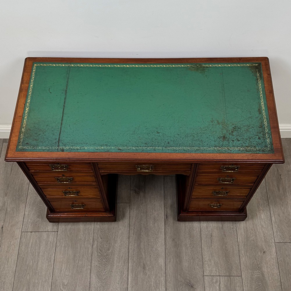 An Edwardian mahogany pedestal desk featuring nine reeded drawers with decorative brass drop handles and a central kneehole. View IX